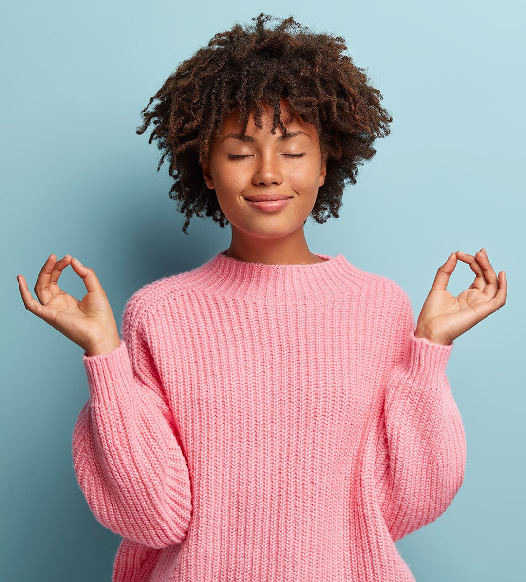 People, peace and meditation concept. Calm black young woman practices yoga indoor, shows okay sign with both hands, demonstrates approval, wears pink clothing, isolated over blue background